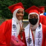 两位毕业生对着头戴礼袍的照片微笑.