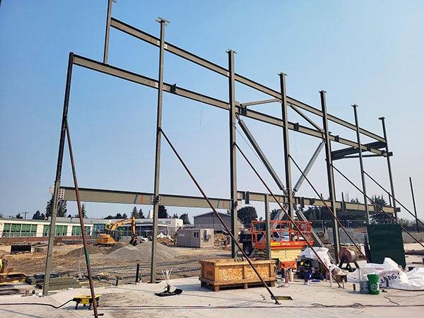 a structural steel frame rises above concreate with a building in the background