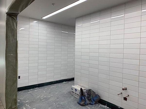 white rectagular tiles cover two walls with a space between them