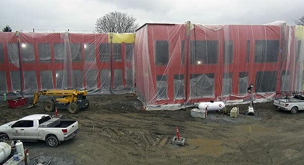 a 2-story building under construction with plastic draped over it - the walls are orange, there are empty spaces for windows, and there is dirt and construction equipment in front