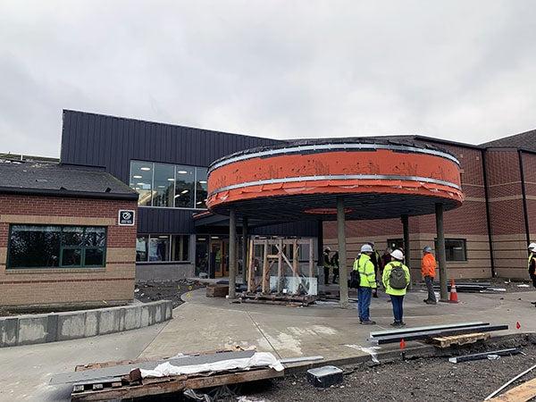 a brick building has a round canopy with orange sheathing. construction workers and materials are in the photo