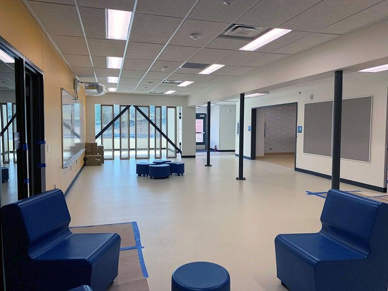 a large space has seating clusters, support poles, and screening from the main hallway
