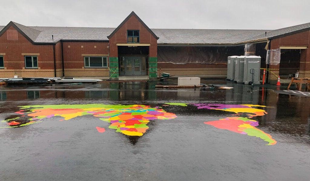 a brick building has a world map painted on the blacktop in front of it