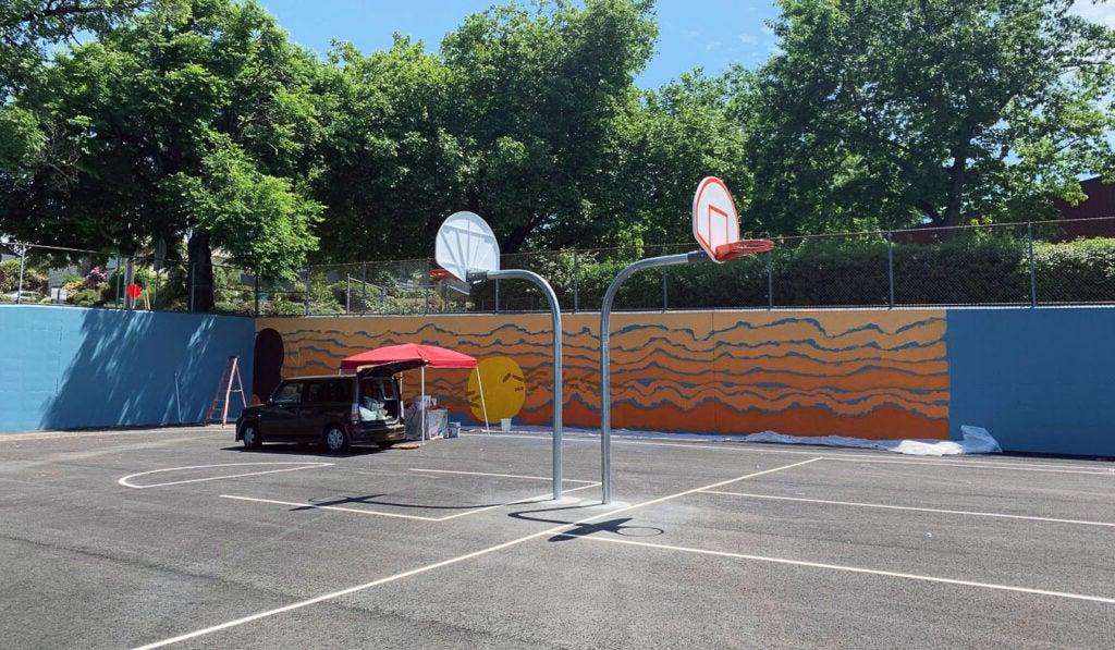 a mural is being painted on a blue wall surrounding a basketball court