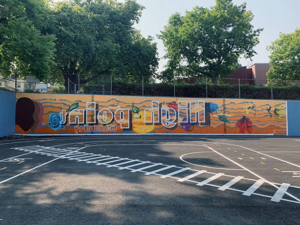 the wall of a paved play area has a mural painted on it that says High Point Community