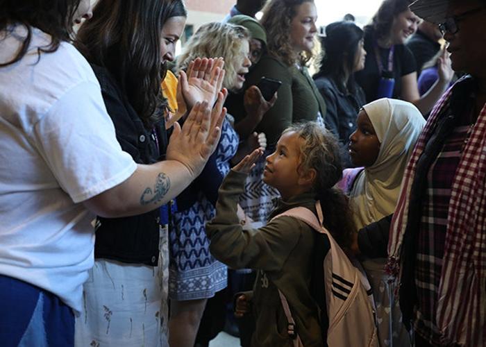 a child in a crowd of several children high fives an adult in a white shirt